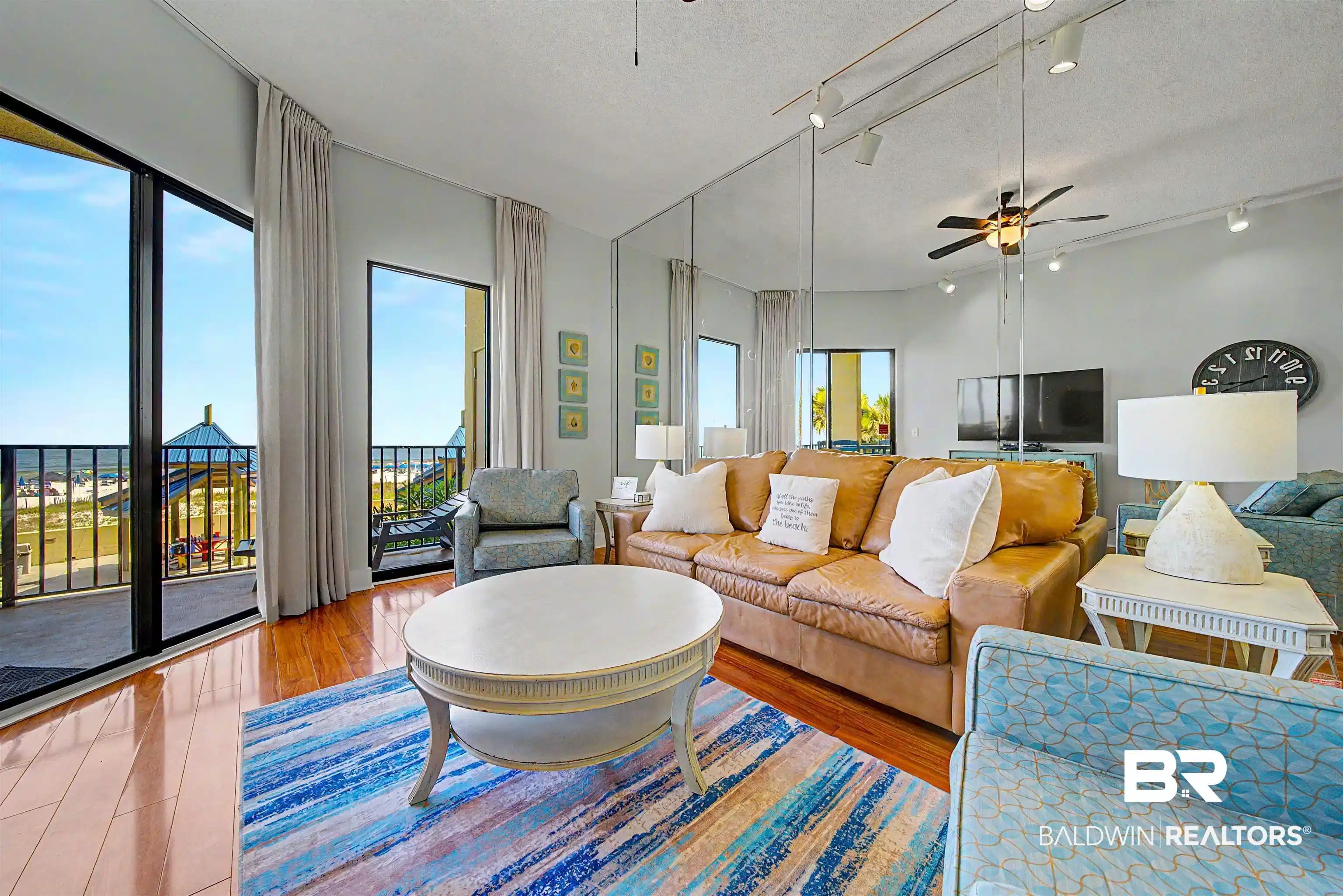 Image 1: Living area featuring wood-finish flooring, full-height sliding glass doors opening to a balcony, a ceiling fan with integrated lighting, and mirrored wall panels