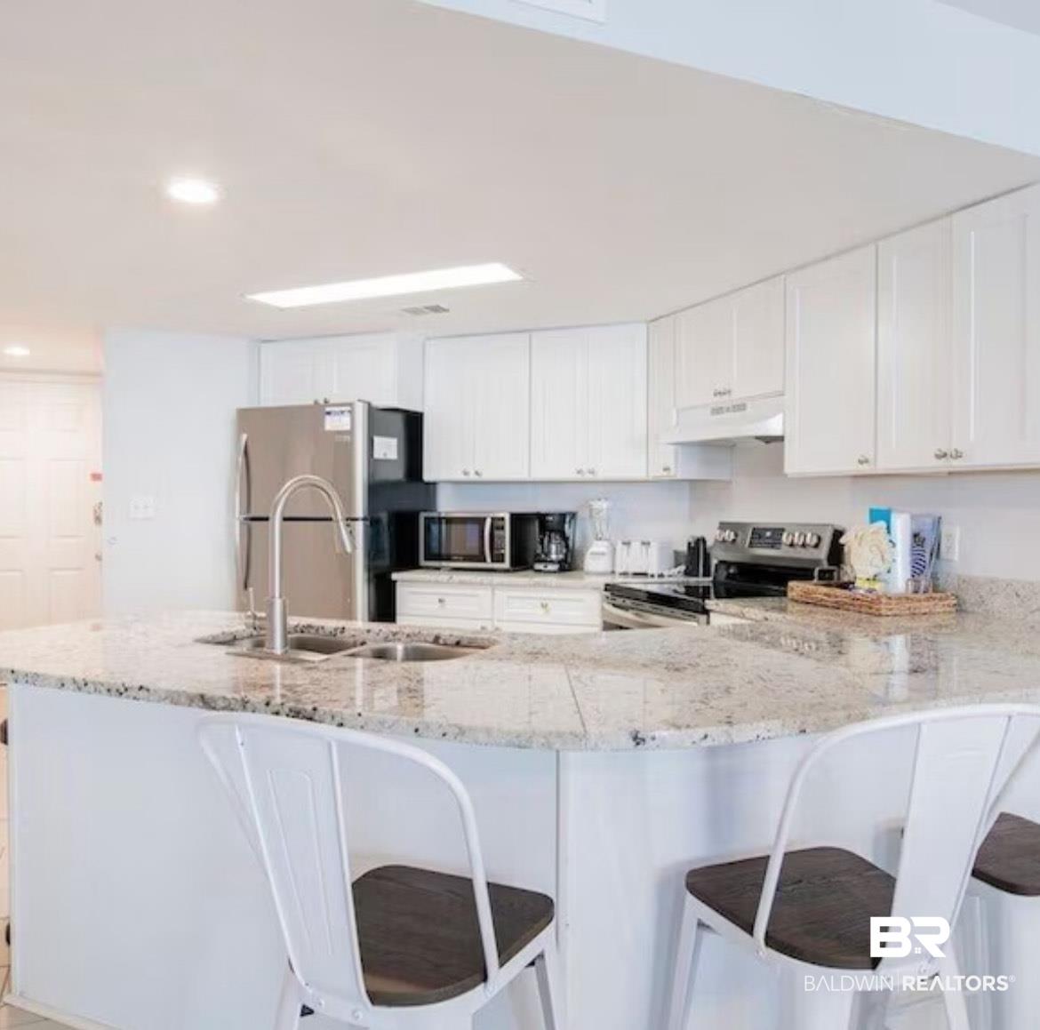 Image 3: Kitchen with white cabinetry, stainless steel appliances, a kitchen bar, and recessed lighting