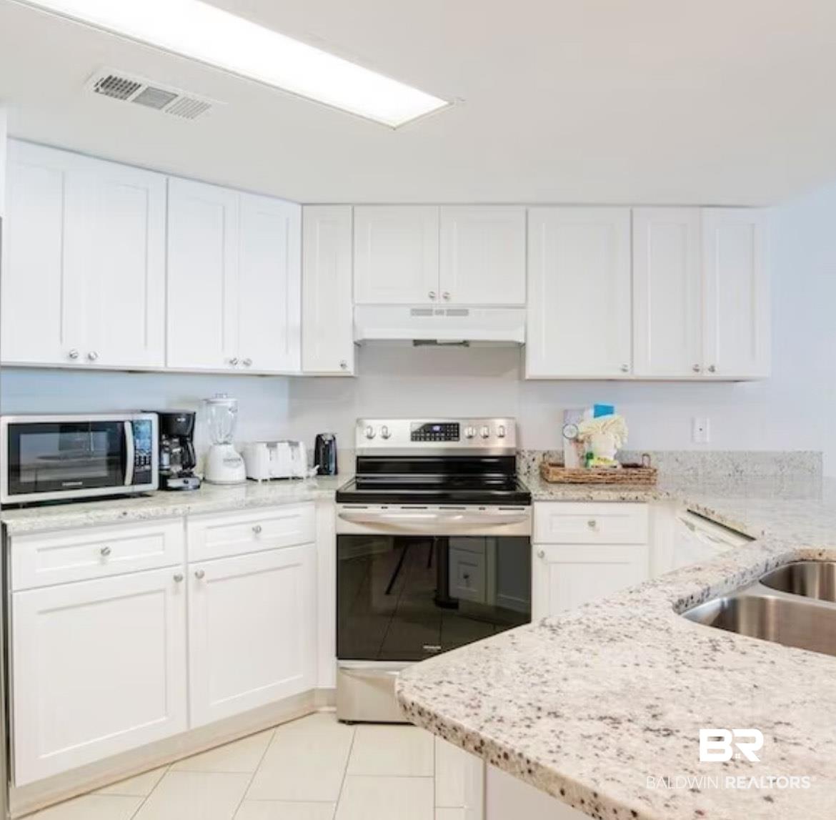 Image 4: Kitchen featuring appliances with stainless steel finishes, light stone counters, white cabinets, under cabinet range hood, and light tile patterned flooring