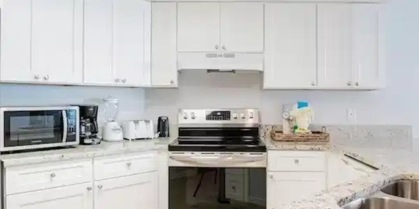 Image 4: Kitchen featuring appliances with stainless steel finishes, light stone counters, white cabinets, under cabinet range hood, and light tile patterned flooring
