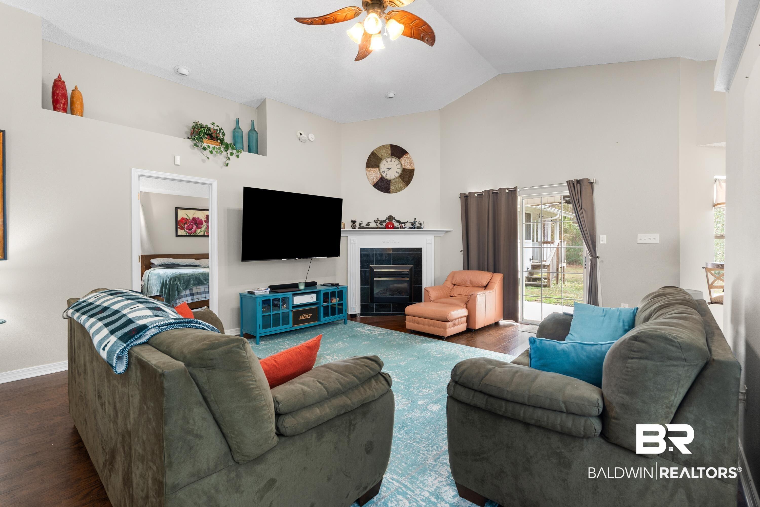 Image 4: Living area with a tiled fireplace, a ceiling fan, wood finished floors, and high vaulted ceiling