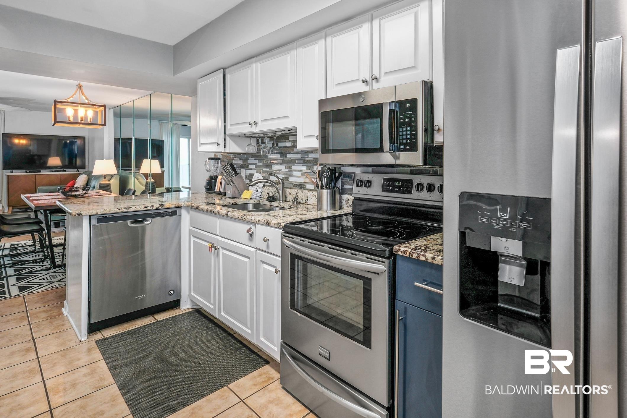 Image 4: Kitchen featuring appliances with stainless steel finishes, light stone countertops, white cabinets, and a peninsula