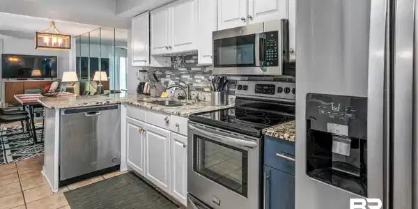 Image 4: Kitchen featuring appliances with stainless steel finishes, light stone countertops, white cabinets, and a peninsula