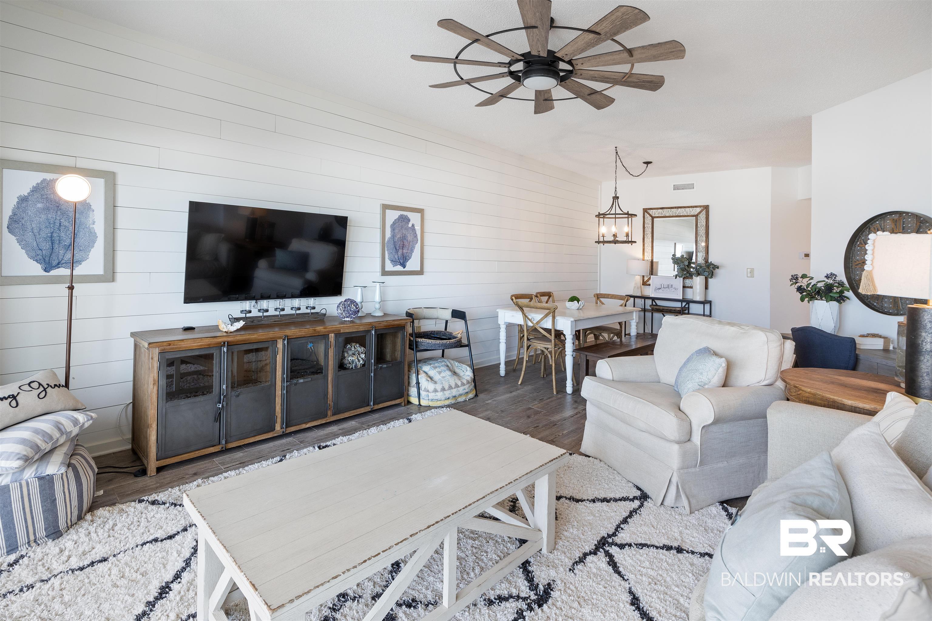 Image 4: Open-concept living area with wood-finish flooring, shiplap accent wall, and a rustic-style ceiling fan