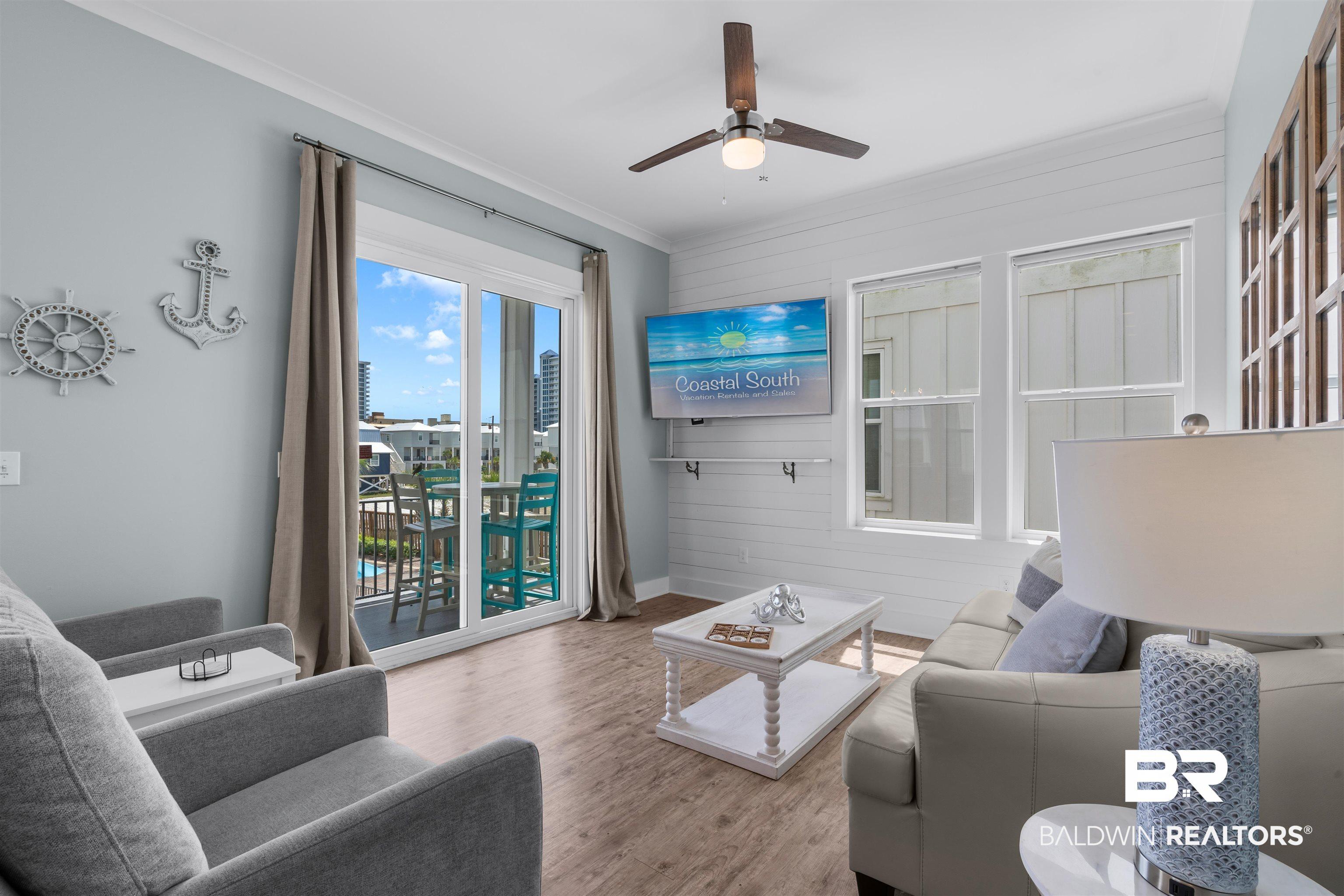 Image 4: Living area featuring wood-finish flooring, shiplap accent wall, ceiling fan, and sliding glass door leading to an outdoor balcony