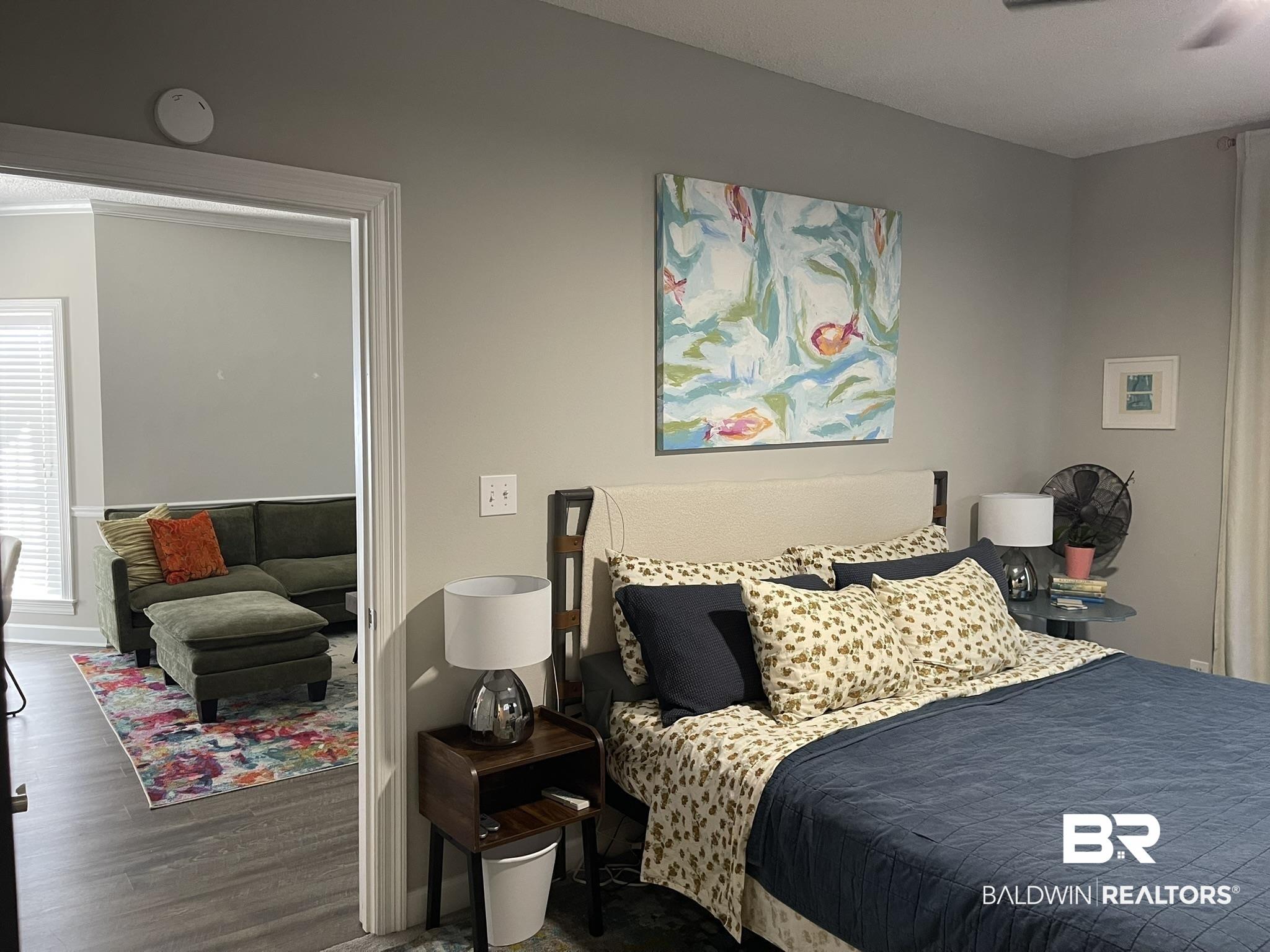 Image 4: Bedroom featuring a cream upholstered headboard, a dark wood-finish nightstand, and light gray wall paint