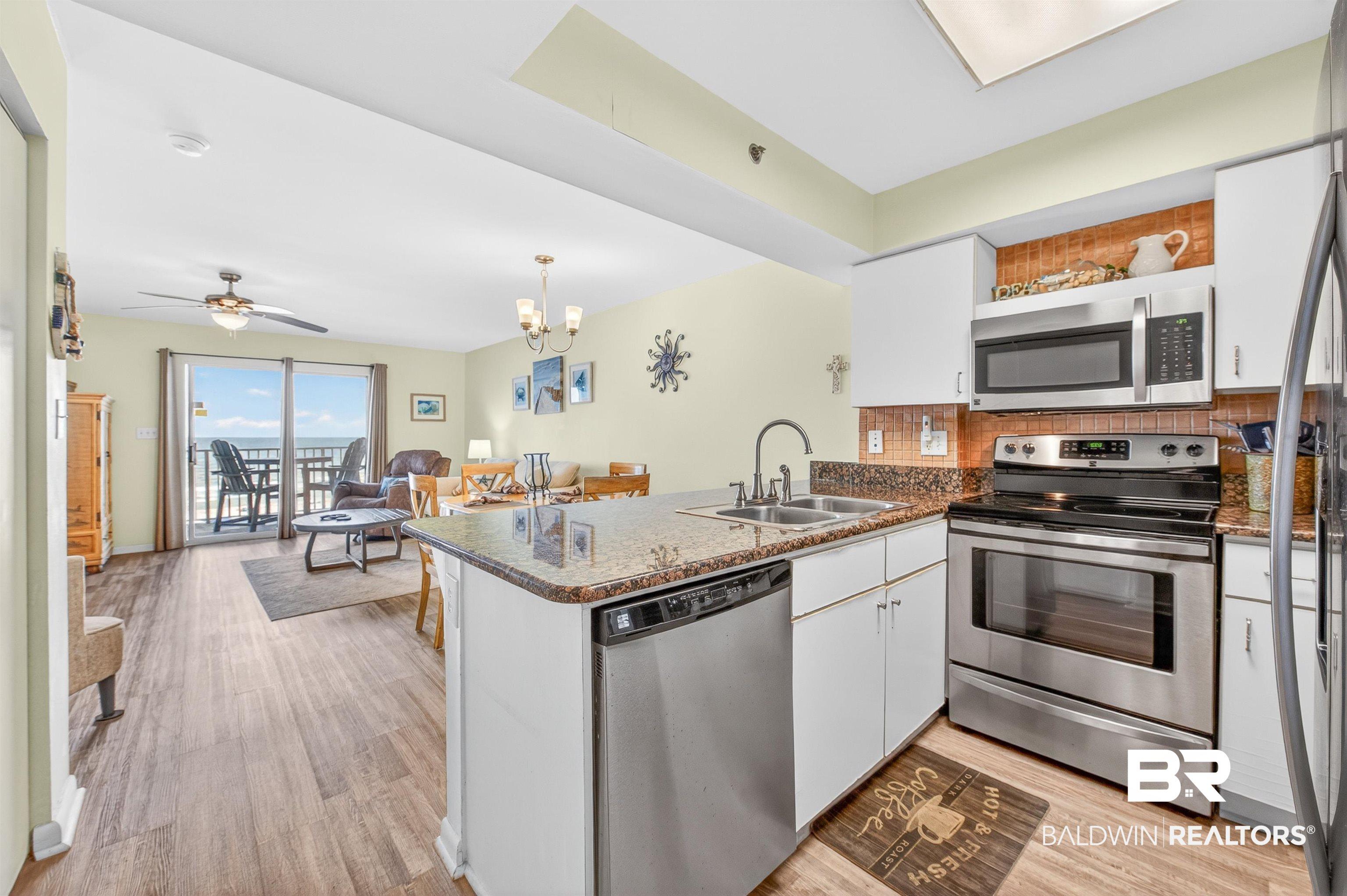 Image 2: Open-concept kitchen featuring white cabinetry, stainless steel appliances, granite countertops, and a tile backsplash