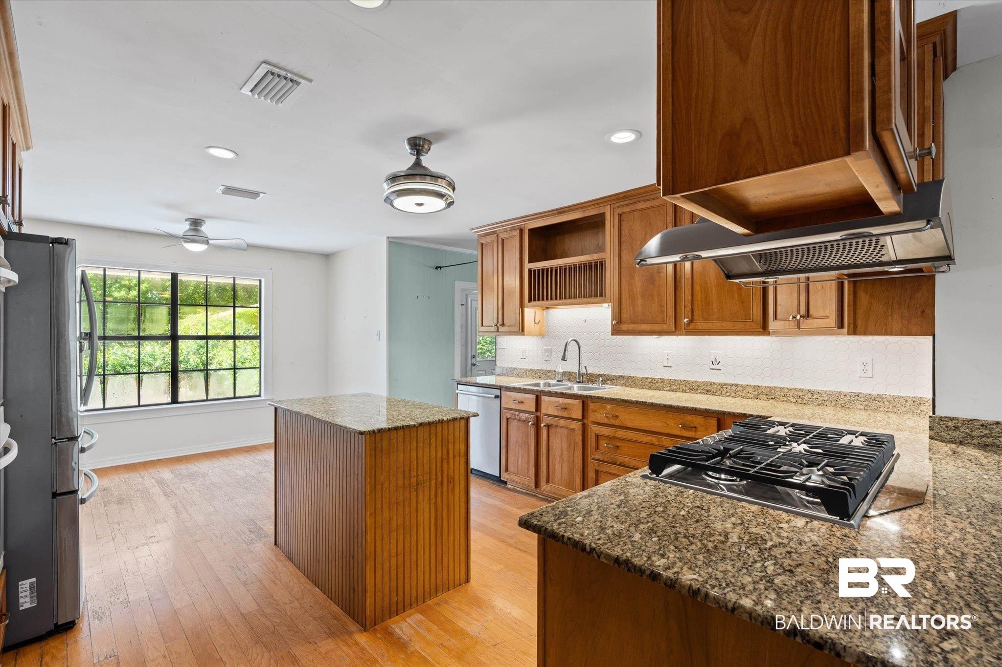 Image 3: Featuring wood-stained cabinets, new gas cooktop, double oven, stainless vent hood, refrigerator, & dishwasher