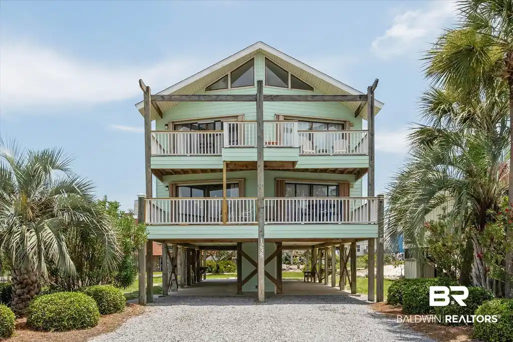 Image 1: Elevated coastal residence featuring two levels of private balconies, a gabled roofline with upper-level windows, and a gravel driveway