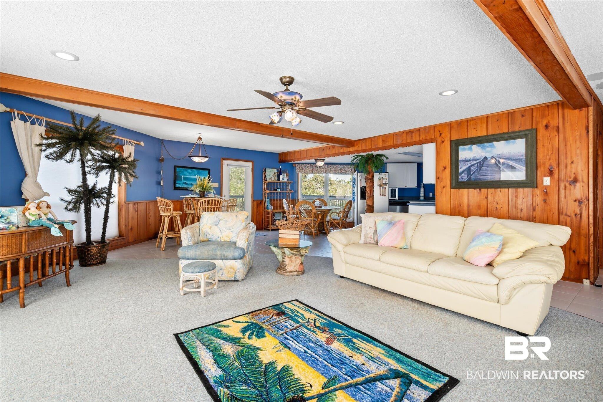 Image 3: Living room with beam ceiling, wooden walls, light colored carpet, a textured ceiling, and ceiling fan