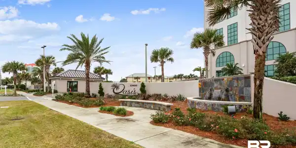 Image 3: Property entrance featuring a stone-clad fountain, stone benches, palm trees, and a decorative sign