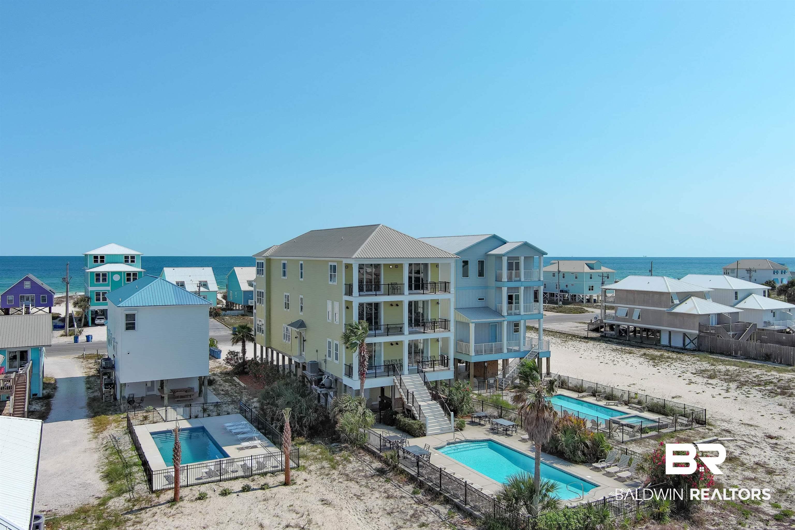 Image 4: Coastal-style architecture featuring multiple balconies, a metal roof, two outdoor swimming pools, and a separate single-story pool with a surrounding fence