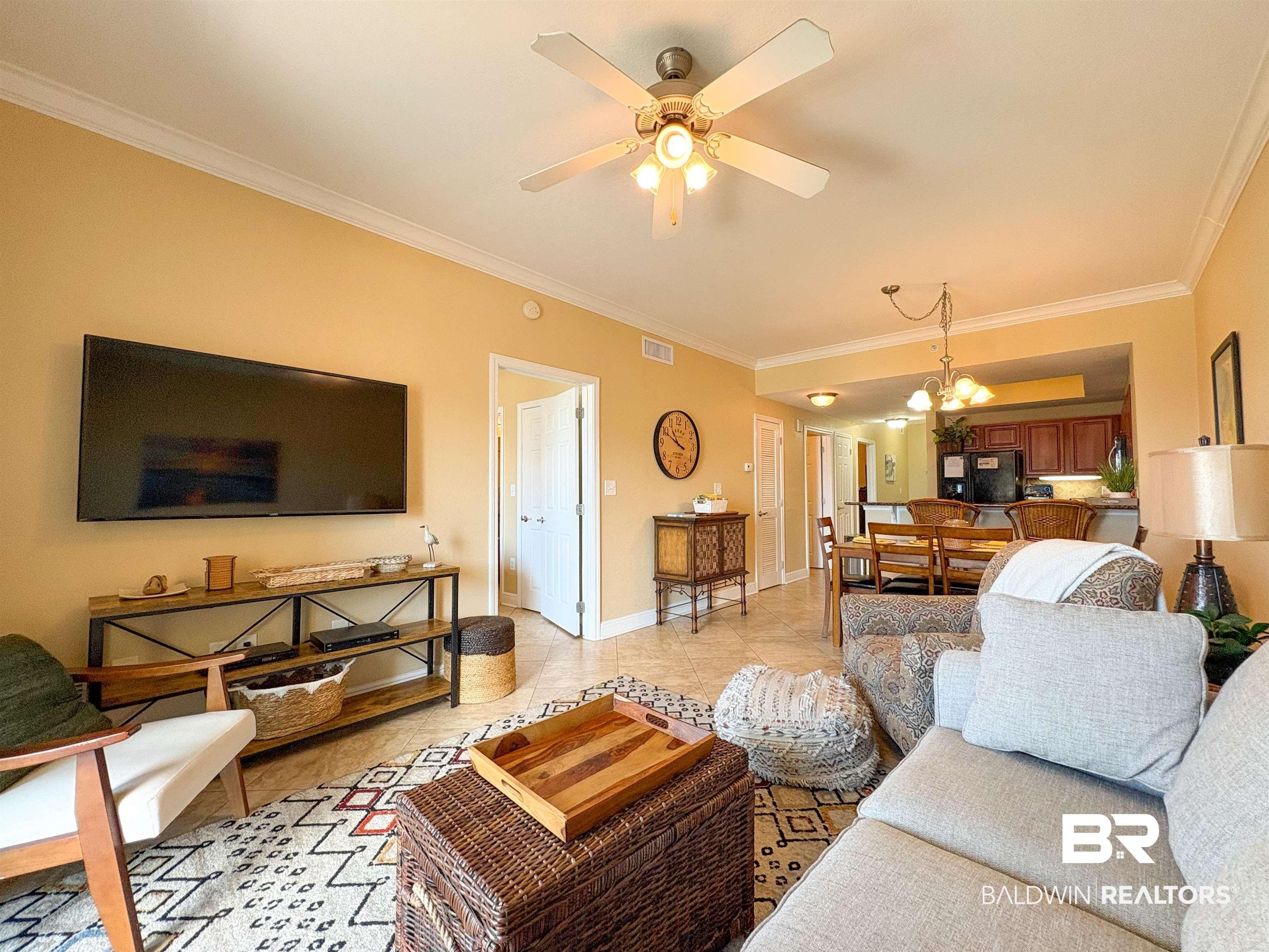 Image 4: Living room with crown molding, visible vents, light tile patterned flooring, baseboards, and ceiling fan with notable chandelier