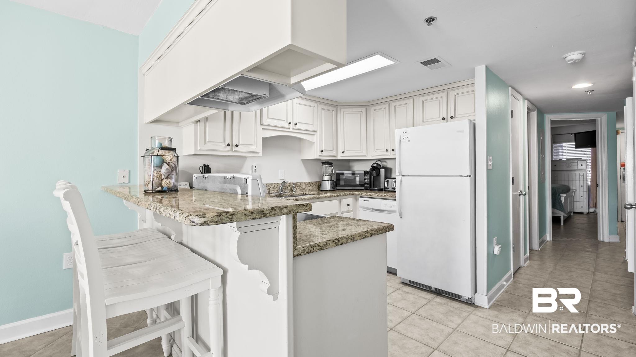 Image 4: Kitchen with a peninsula, white appliances, dark stone countertops, a breakfast bar, and white cabinets