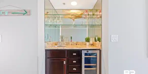 Image 4: Indoor wet bar with dark wood finish cabinetry, wine cooler, and light stone counters