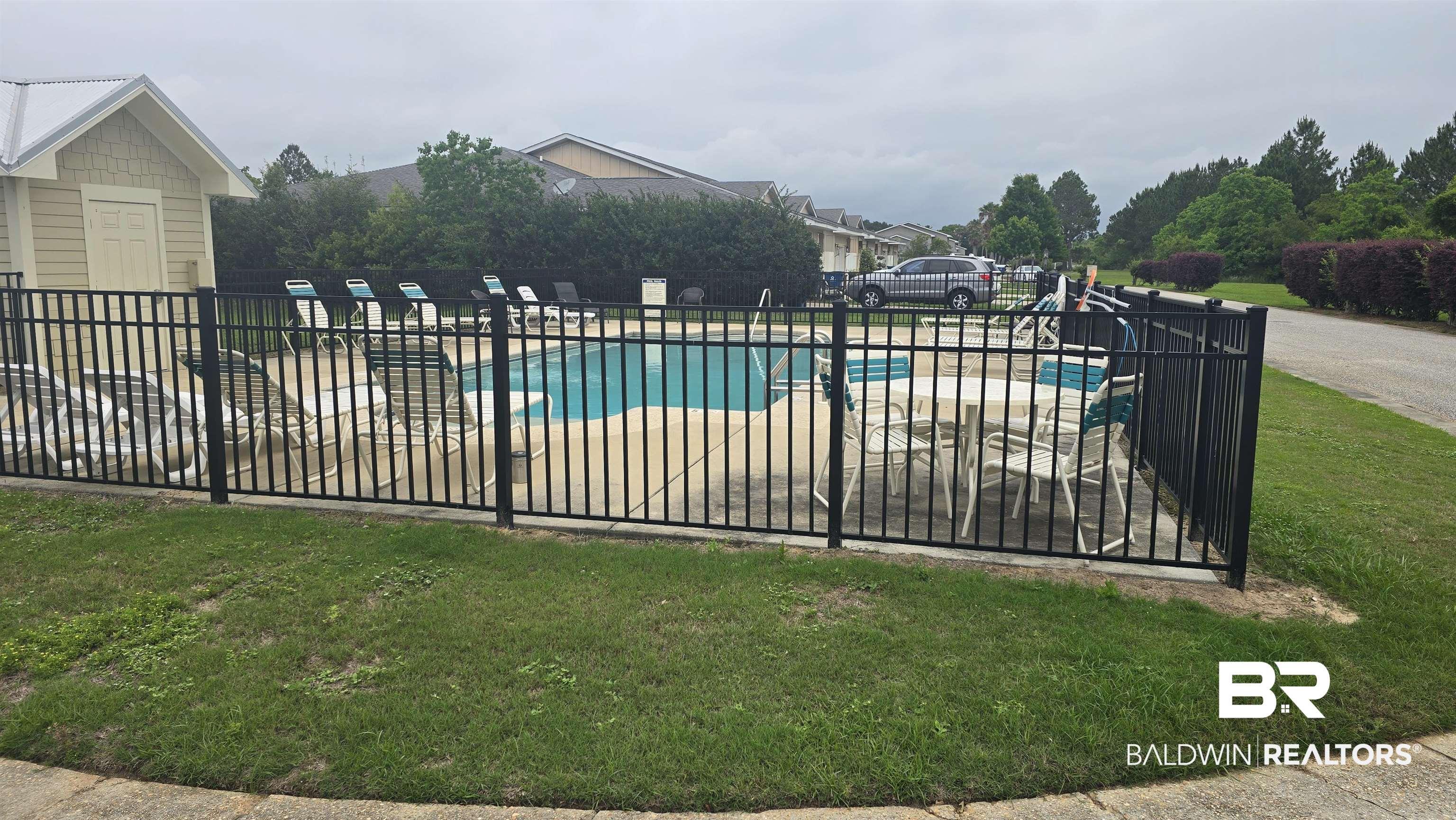 Image 2: Outdoor swimming pool with surrounding concrete patio, black metal fencing, and a nearby pool house featuring horizontal siding and a white metal roof
