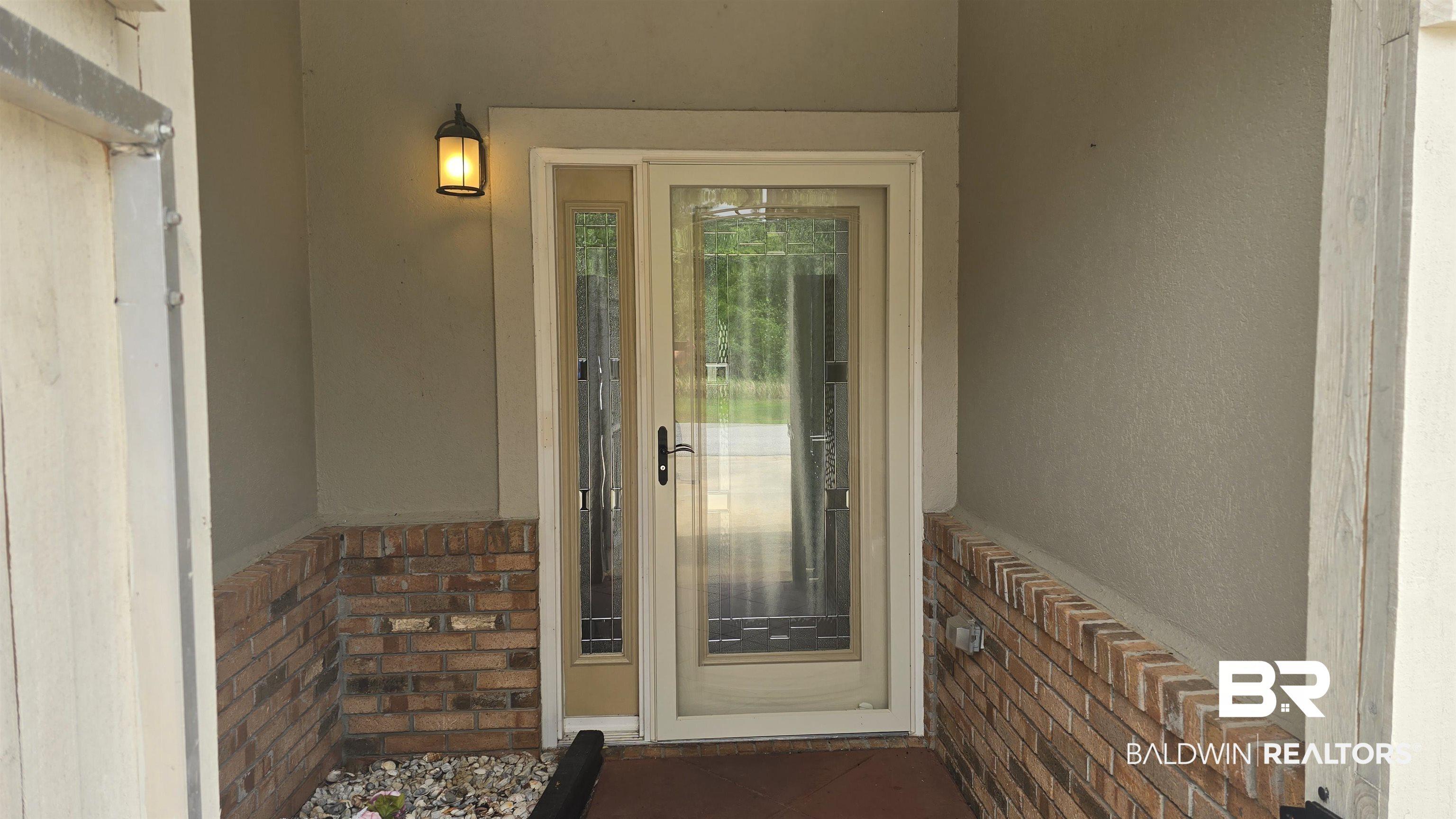 Image 4: Entryway featuring a decorative glass storm door, an exterior wall sconce, and a brick wainscoting detail