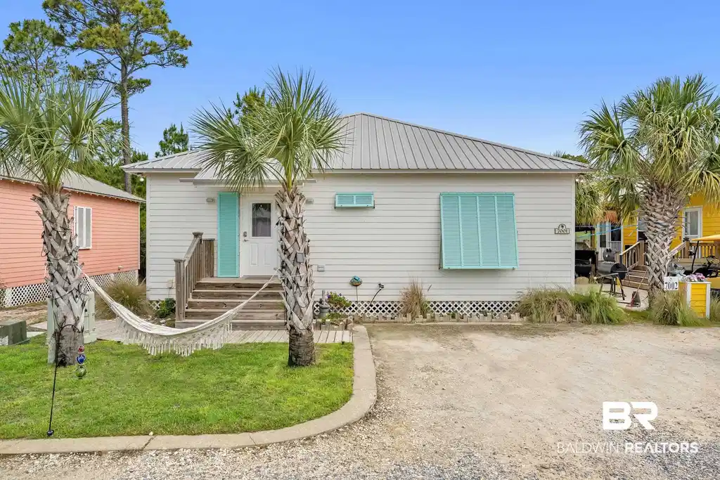 Image 1: White siding exterior featuring a metal roof, turquoise front door, and matching window awnings