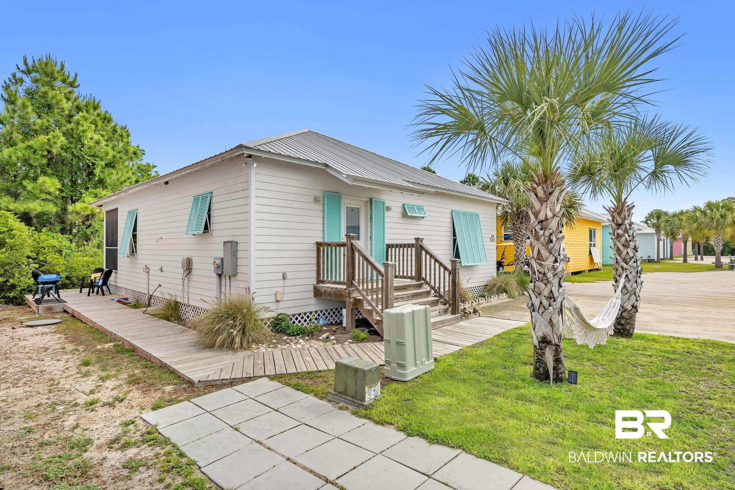 Image 3: White exterior siding with turquoise shutters, a front porch with wood railings, a metal roof, and two mature palm trees
