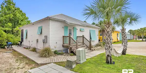 Image 3: White exterior siding with turquoise shutters, a front porch with wood railings, a metal roof, and two mature palm trees
