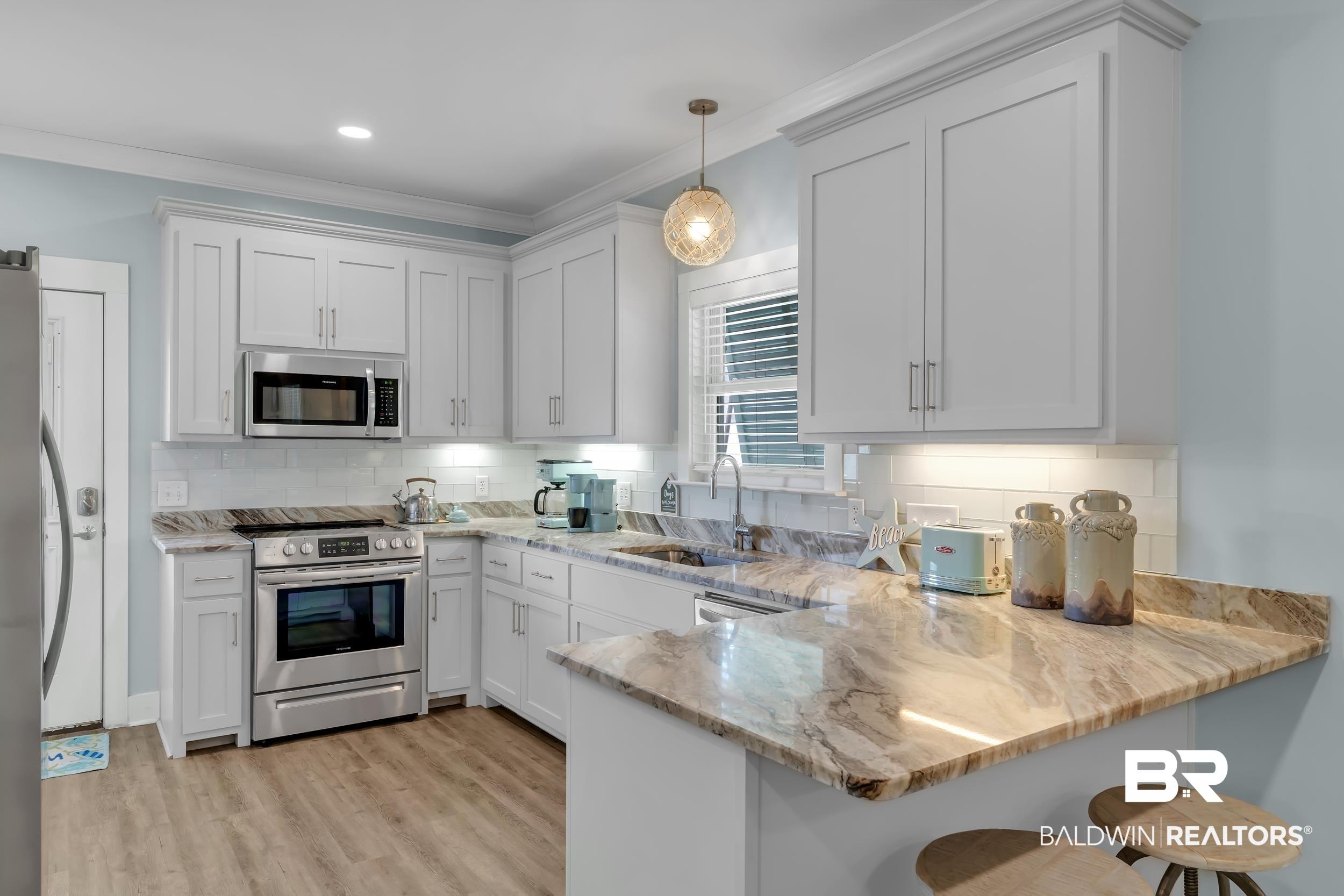 Image 4: Modern kitchen featuring white shaker cabinetry, stainless steel appliances, a subway tile backsplash, light-toned wood-finish flooring, and natural stone countertops with a breakfast bar