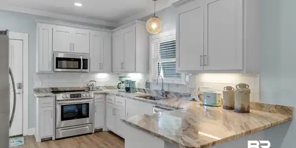 Image 4: Modern kitchen featuring white shaker cabinetry, stainless steel appliances, a subway tile backsplash, light-toned wood-finish flooring, and natural stone countertops with a breakfast bar