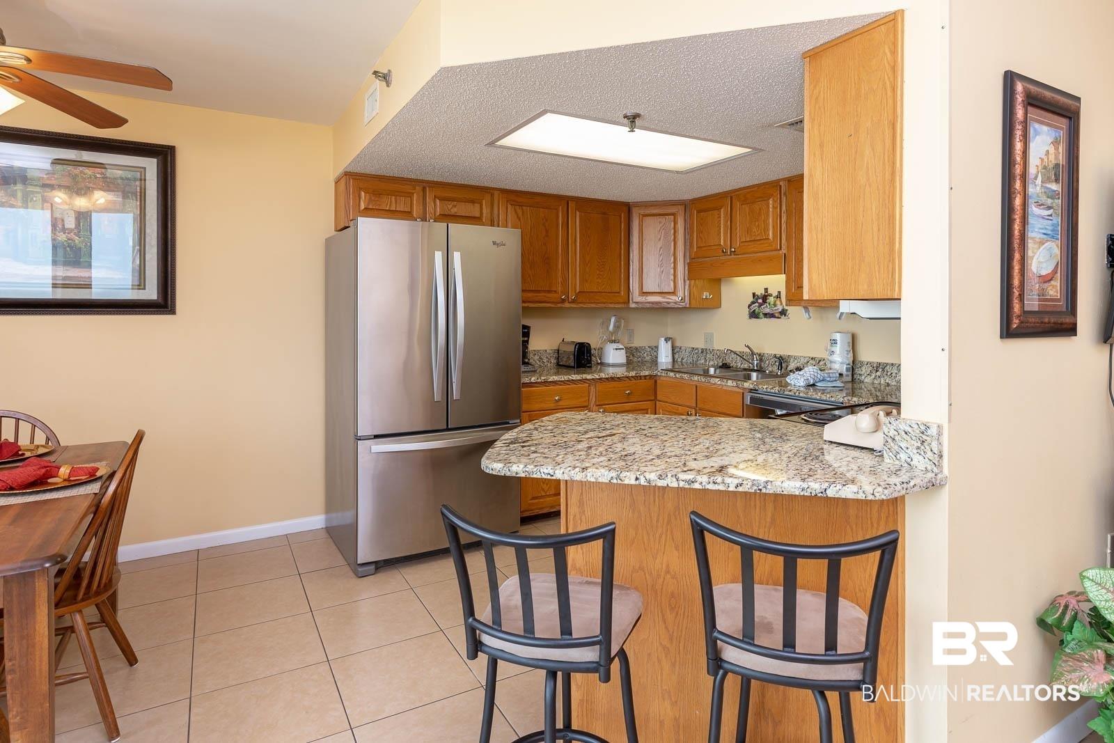 Image 4: Kitchen featuring granite countertops, wood cabinetry, stainless steel appliances, and a breakfast bar with seating