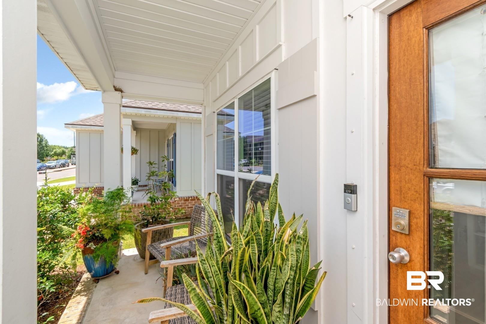 Image 3: Covered porch entry featuring a wood-panel door with glass inserts, white board and batten siding, and a concrete porch floor