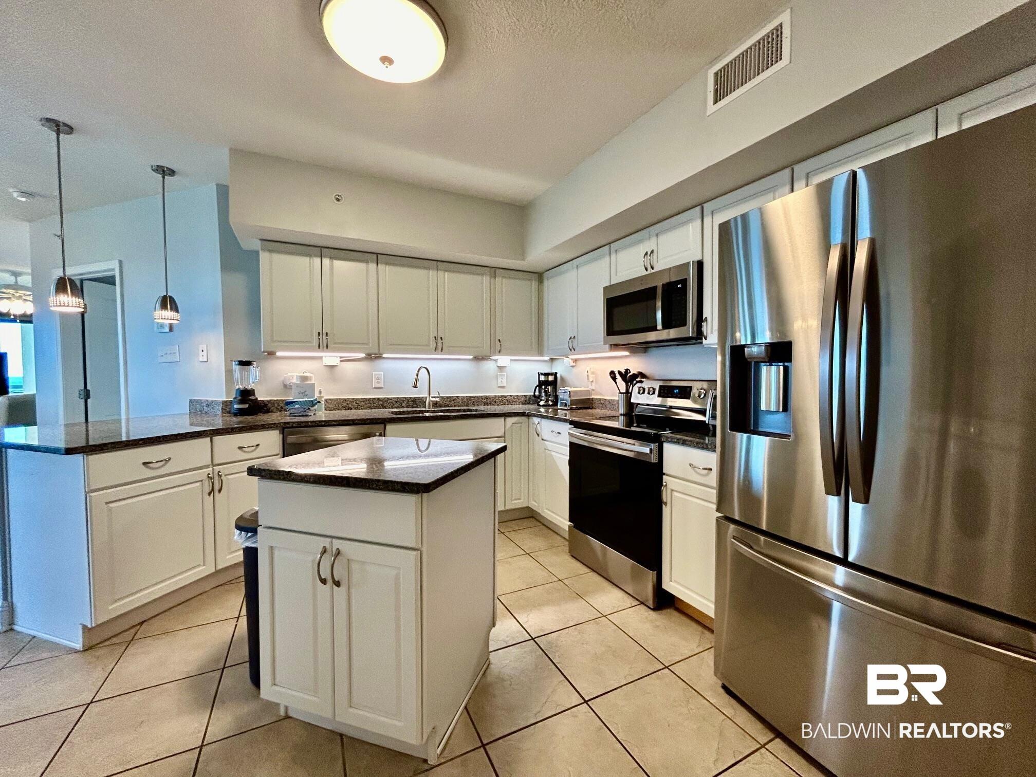 Image 3: Kitchen with appliances with stainless steel finishes, dark stone countertops, white cabinets, and a textured ceiling