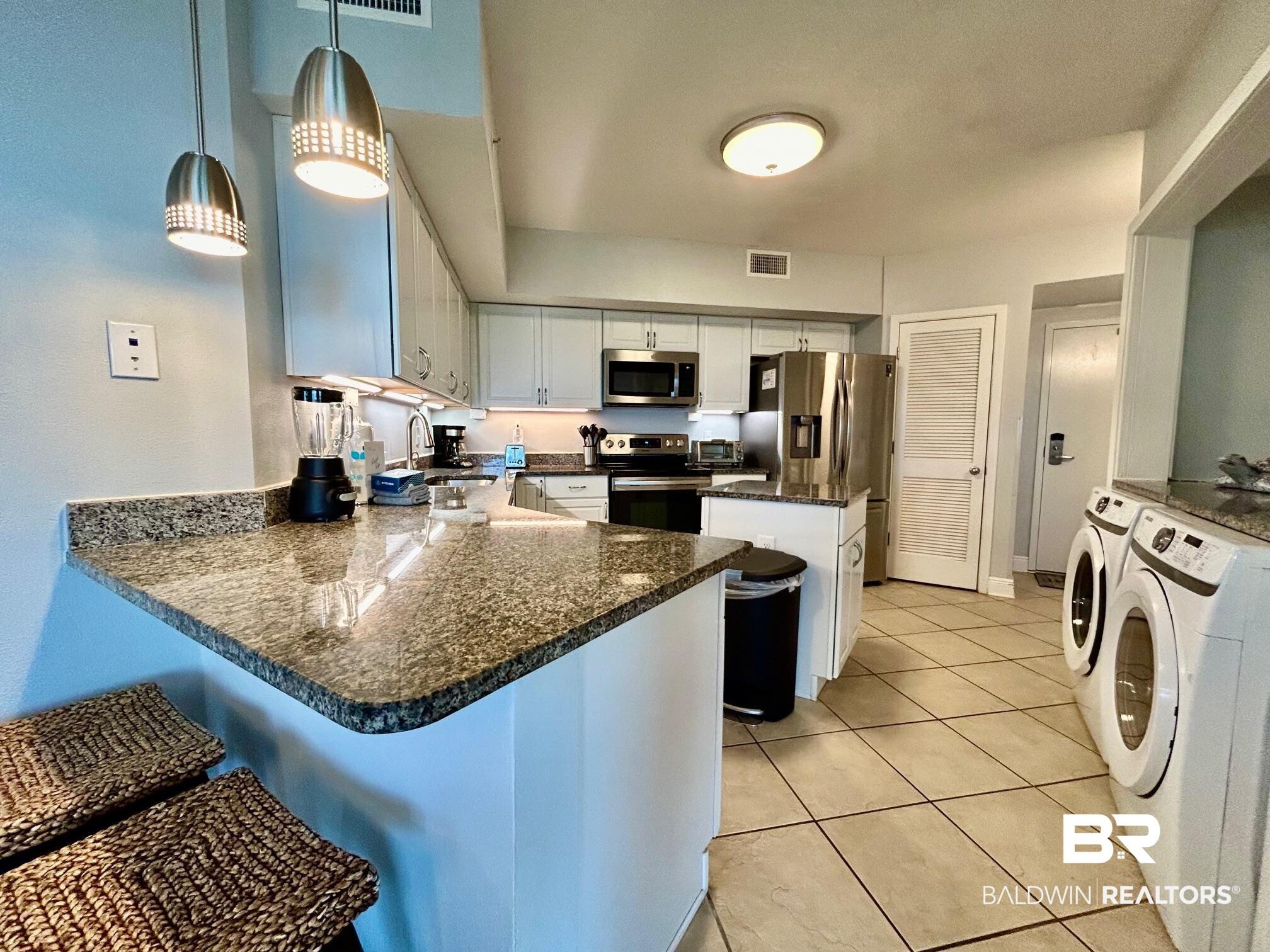 Image 4: Kitchen featuring white cabinets, a kitchen bar, appliances with stainless steel finishes, decorative light fixtures, and washing machine and clothes dryer