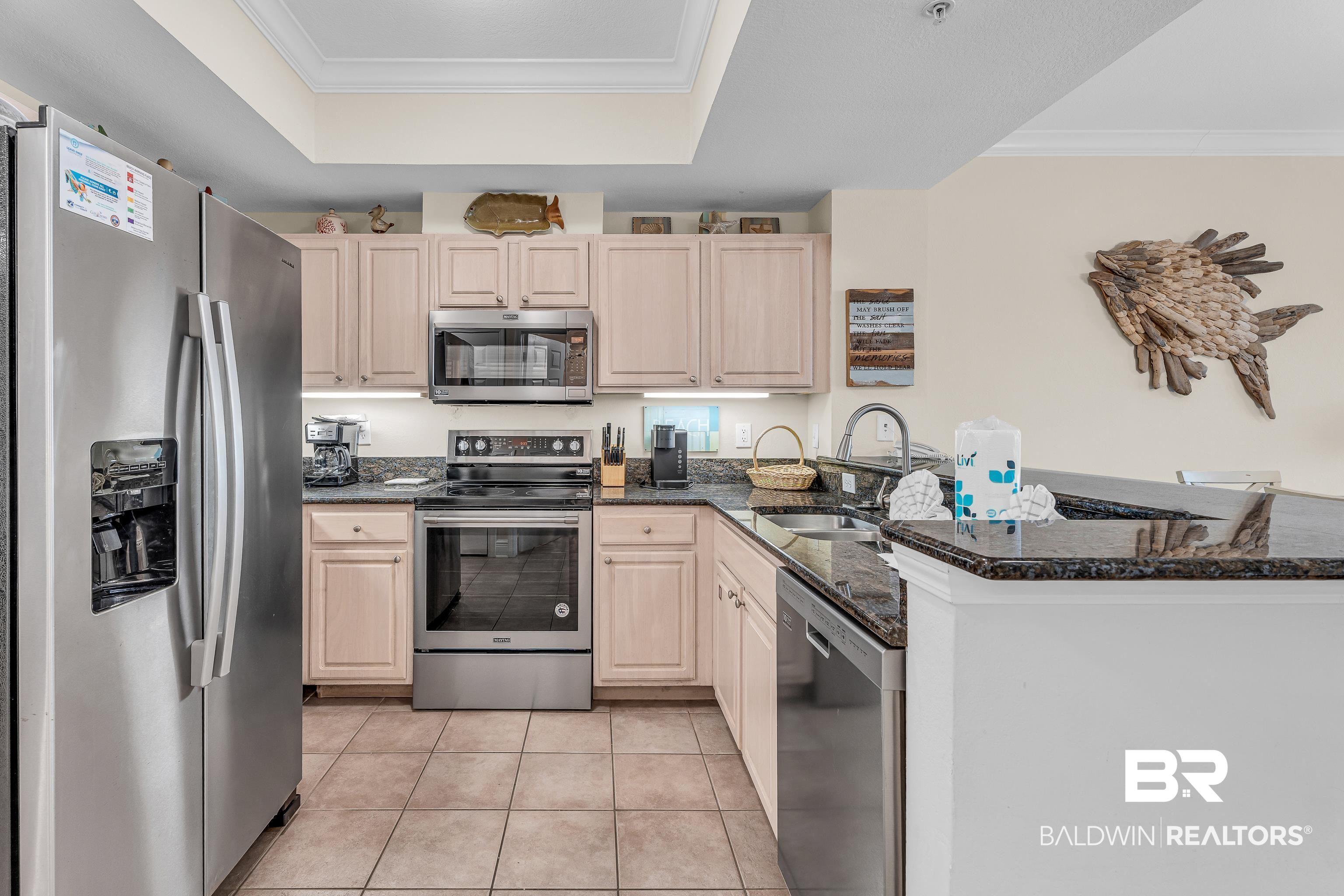 Image 2: Kitchen with stainless steel appliances, crown molding, dark stone counters, light wood finish cabinets, and light tile patterned flooring