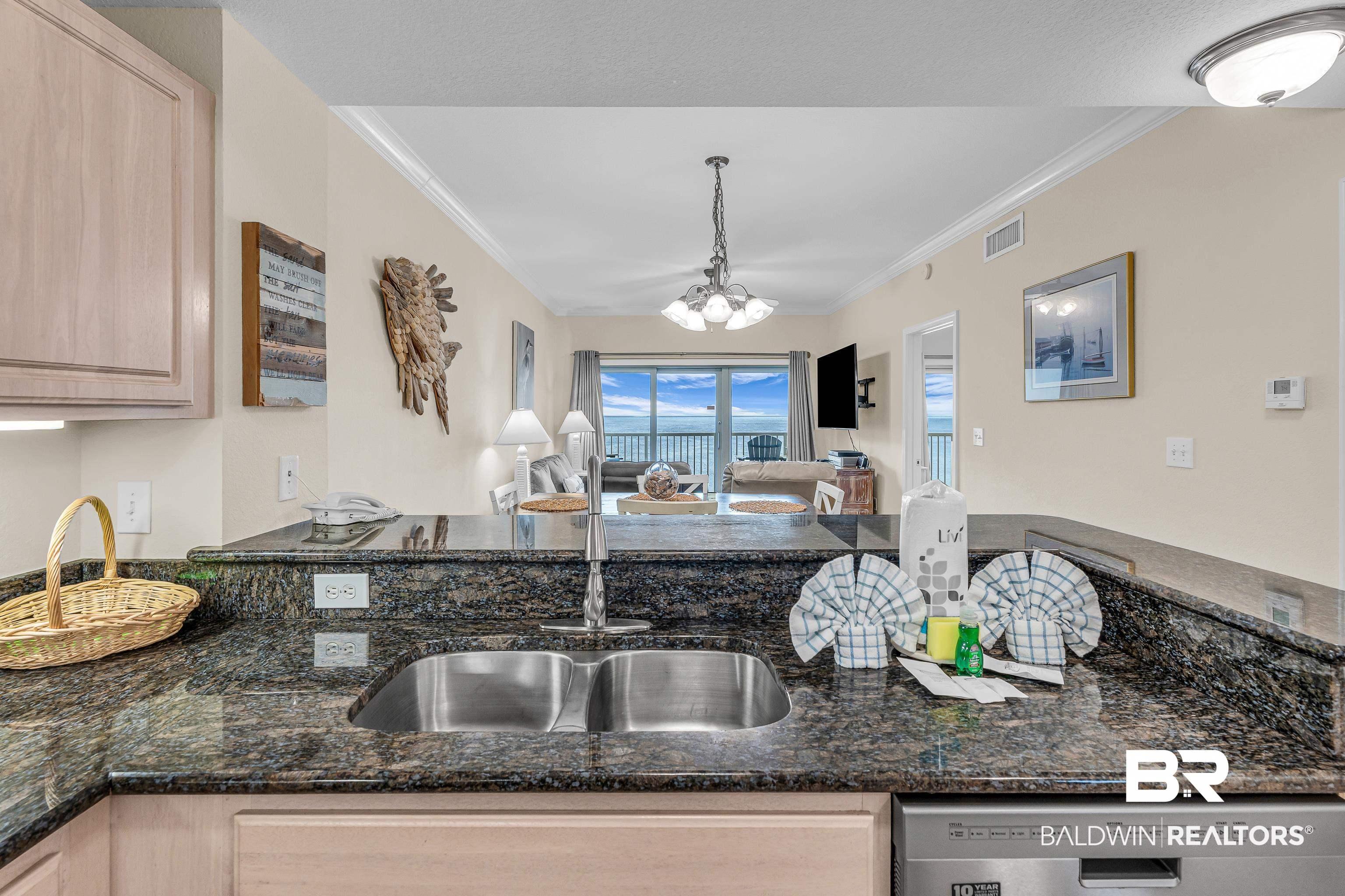 Image 3: Kitchen with light wood finish cabinets, open floor plan, dark stone countertops, suspended lighting, and ornamental molding