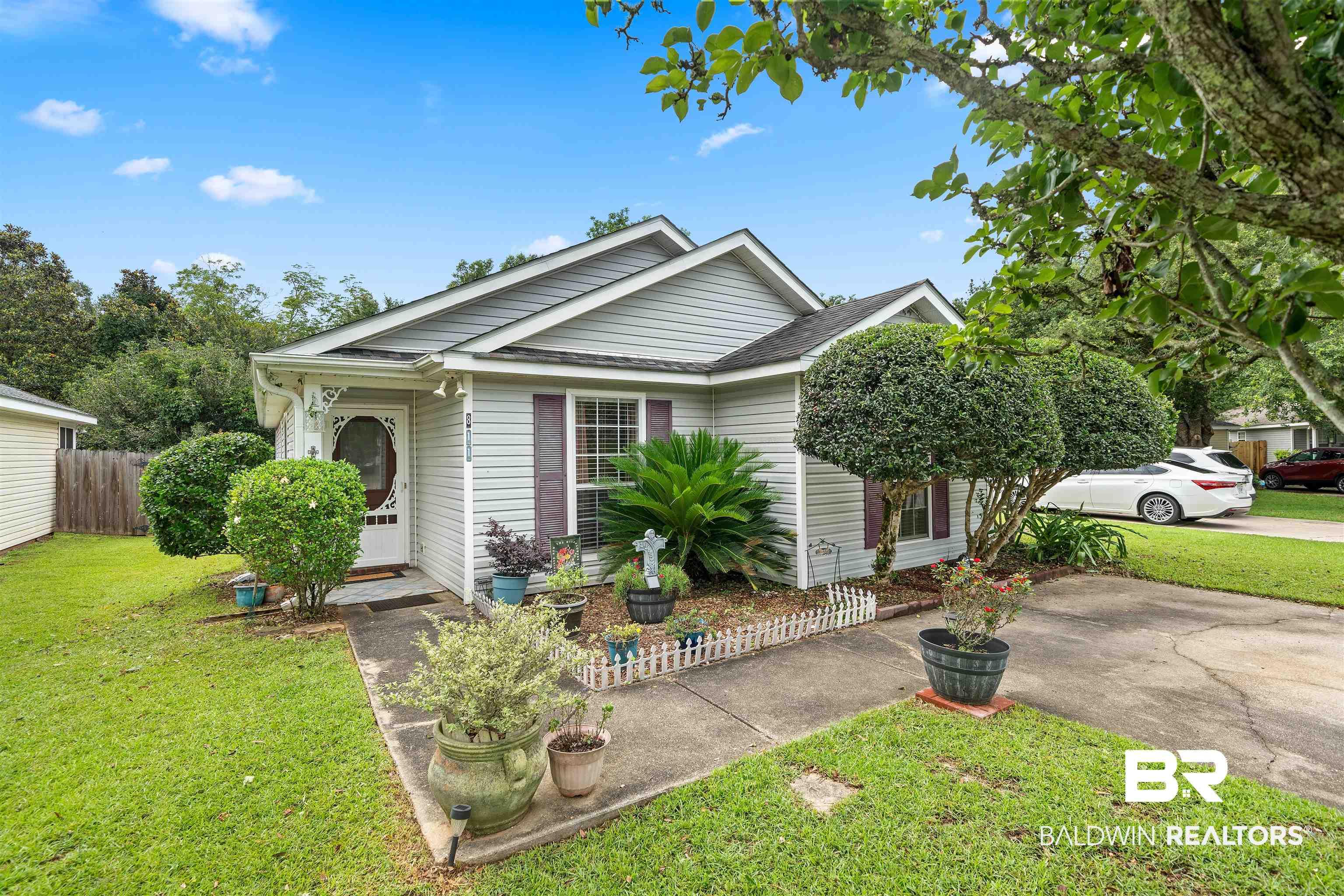 Image 2: Light gray horizontal siding exterior with a white storm door, front yard landscaping, concrete driveway, and a paved walkway