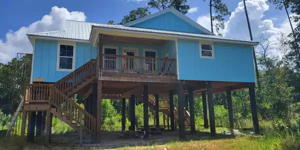 Image 2: Stilt foundation residence featuring blue vertical siding and a metal roof