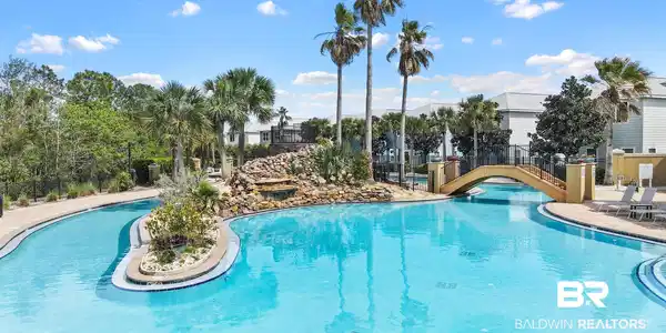 Image 2: Expansive resort-style swimming pool featuring a rock waterfall, a bridge arching over the water, a central landscaped island, and surrounding palm trees