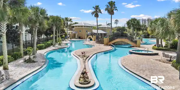Image 3: Expansive resort-style swimming pool featuring a lazy river design, a built-in spa, paver decking, and mature palm trees