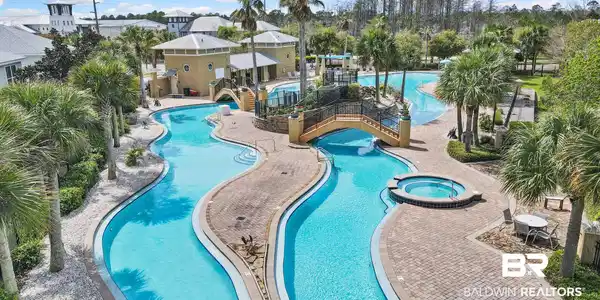 Image 4: Expansive community pool area featuring a lazy river, integrated spa, multiple bridges, and surrounding palm trees