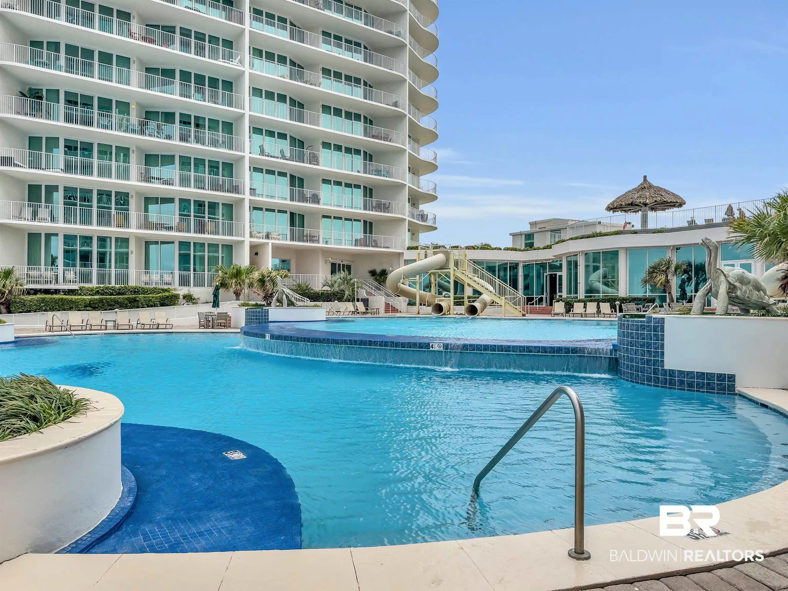 Image 1: Multi-level outdoor pool area featuring a curved swimming pool with a waterfall, a shallow entry, and blue tile accents