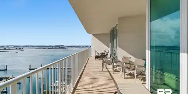 Image 3: Expansive balcony featuring water frontage, white railing, floor-to-ceiling glass sliding doors, and light-toned tile flooring