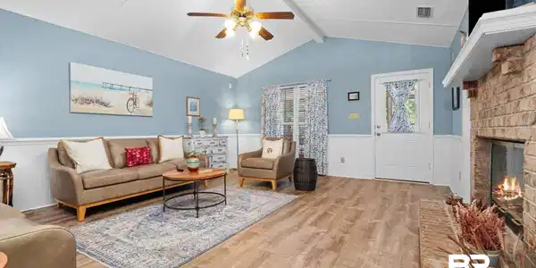 Image 2: Spacious living area featuring wood-finish flooring, a vaulted ceiling with exposed beams, and a ceiling fan