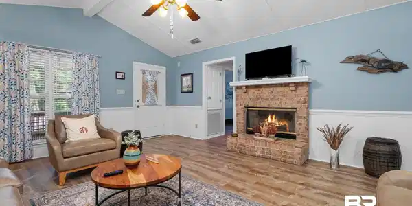Image 4: Living area featuring vaulted ceilings, wood-finish flooring, a brick fireplace, and a ceiling fan with integrated lighting