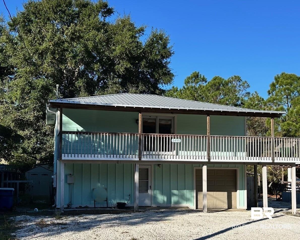 Image 2: View of front of home with an attached garage, gravel driveway, a metal roof, board and batten siding, and a storage unit