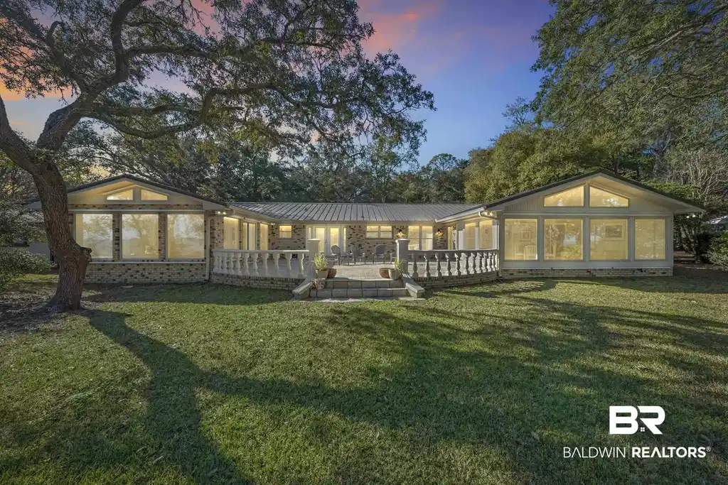 Image 1: Back of property at dusk featuring a sunroom, a metal roof, a yard, and brick siding