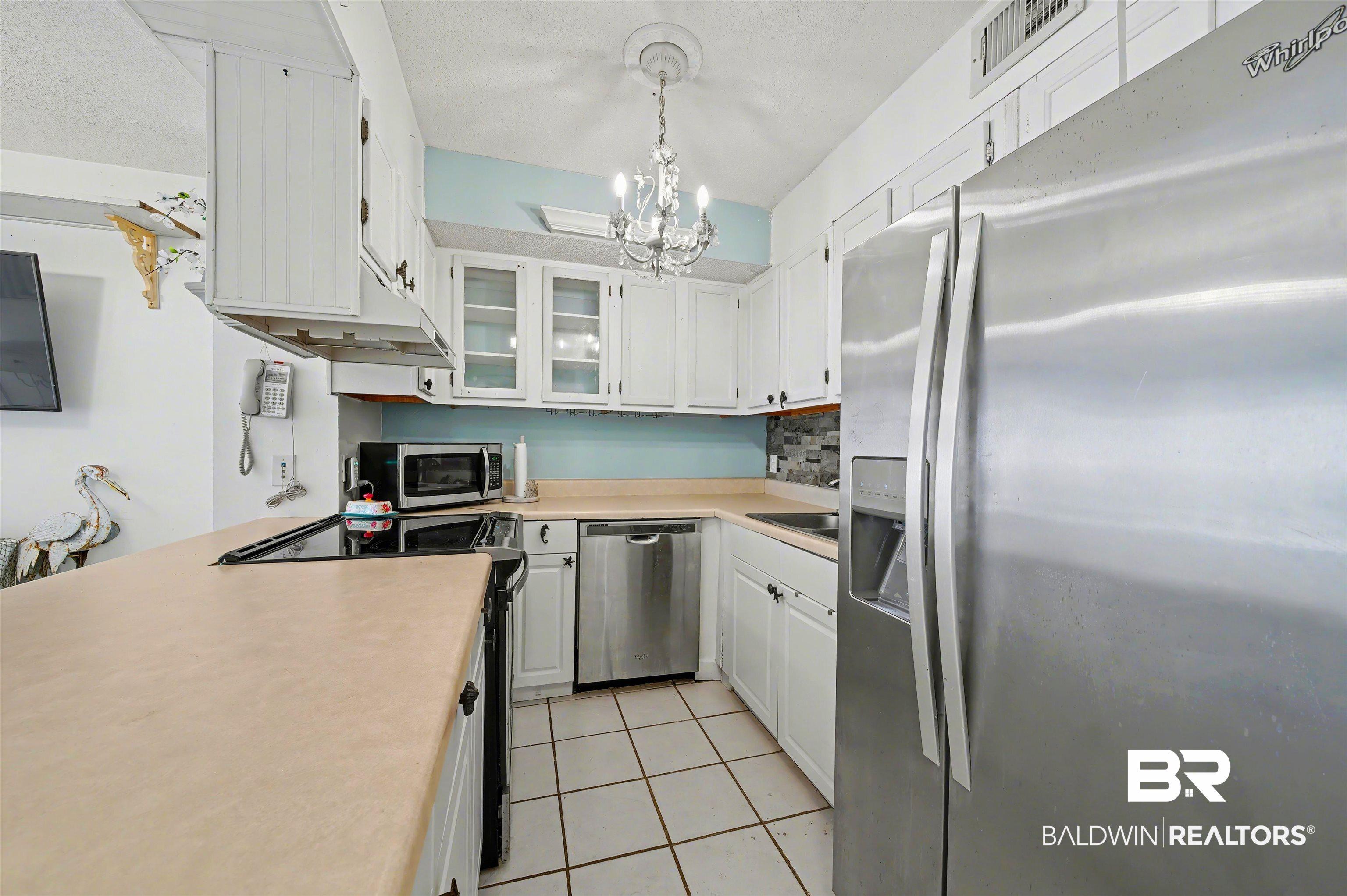 Image 3: Kitchen featuring appliances with stainless steel finishes, white cabinets, light countertops, a chandelier, and light tile patterned floors