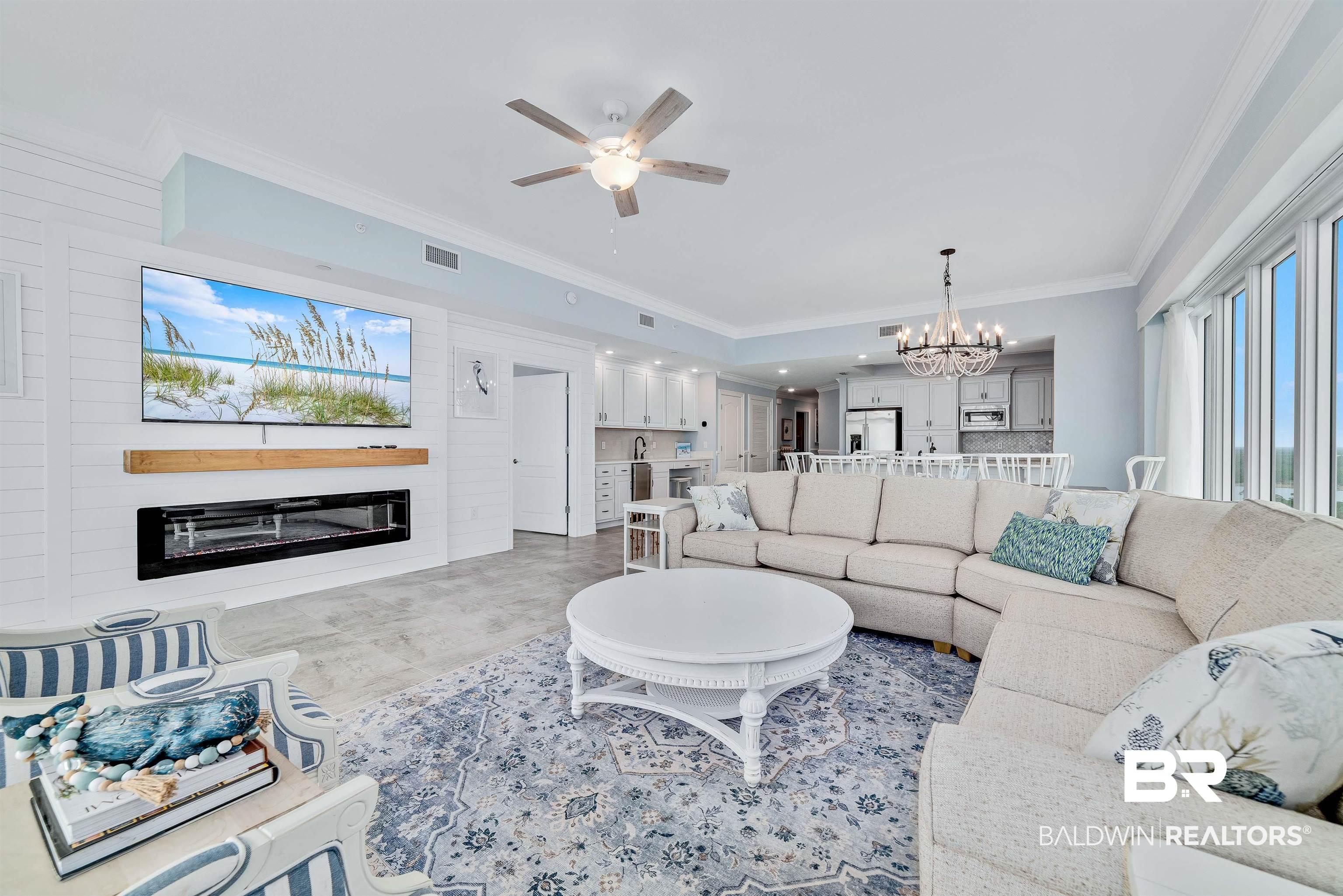 Image 4: Living area featuring crown molding, ceiling fan, suspended lighting, and a glass covered fireplace