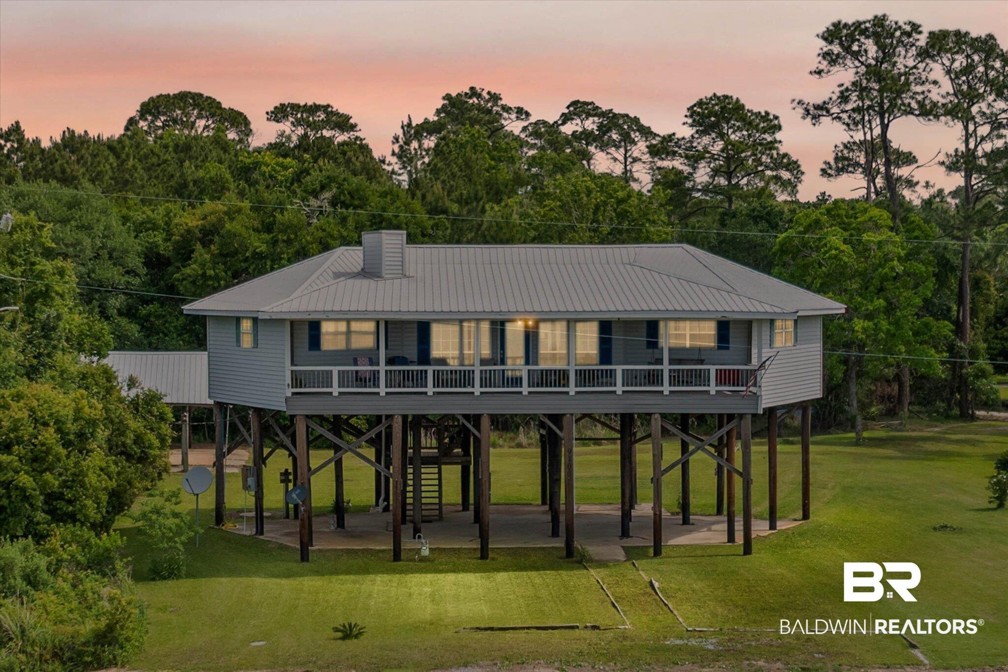 Image 2: Elevated coastal-style residence featuring a metal roof, a full-width covered porch with white railings, and a ground-level covered parking area