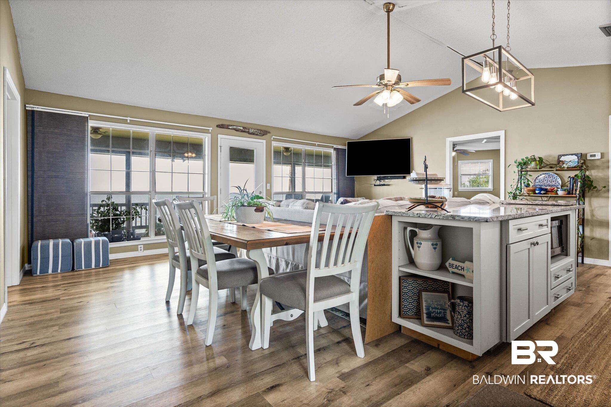 Image 3: Open-concept living space featuring wood-finish flooring, a vaulted ceiling, and an integrated kitchen island with a light-colored countertop