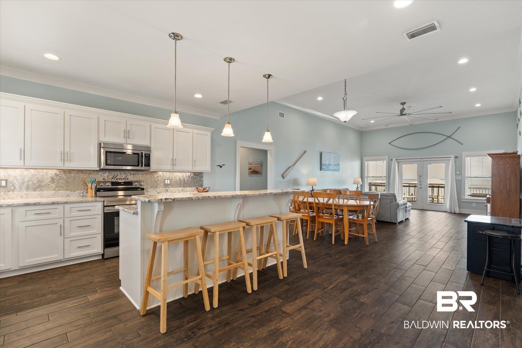 Image 2: Open-concept kitchen and living area featuring wood-finish flooring, white cabinetry, a kitchen island with seating, stainless steel appliances, and French doors