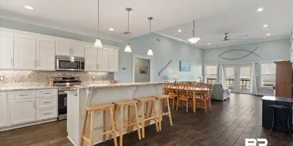 Image 2: Open-concept kitchen and living area featuring wood-finish flooring, white cabinetry, a kitchen island with seating, stainless steel appliances, and French doors