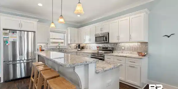 Image 3: Modern kitchen featuring white shaker cabinetry, stainless steel appliances, speckled stone countertops, and wood-finish flooring